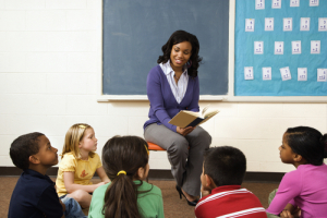 Teacher reading book to young students in classroom. Horizontally framed shot