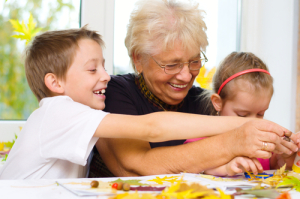 Grandmother with grandchildren applying a dry maple leaves using glue while doing arts and crafts