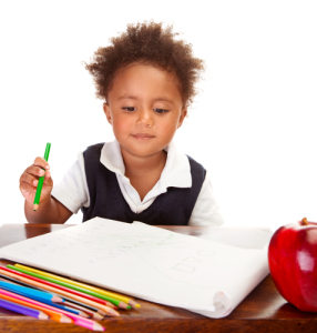 Portrait of cute little African American schoolboy sitting behind the desk and drawing, happy pupil isolated on white background, back to school concept